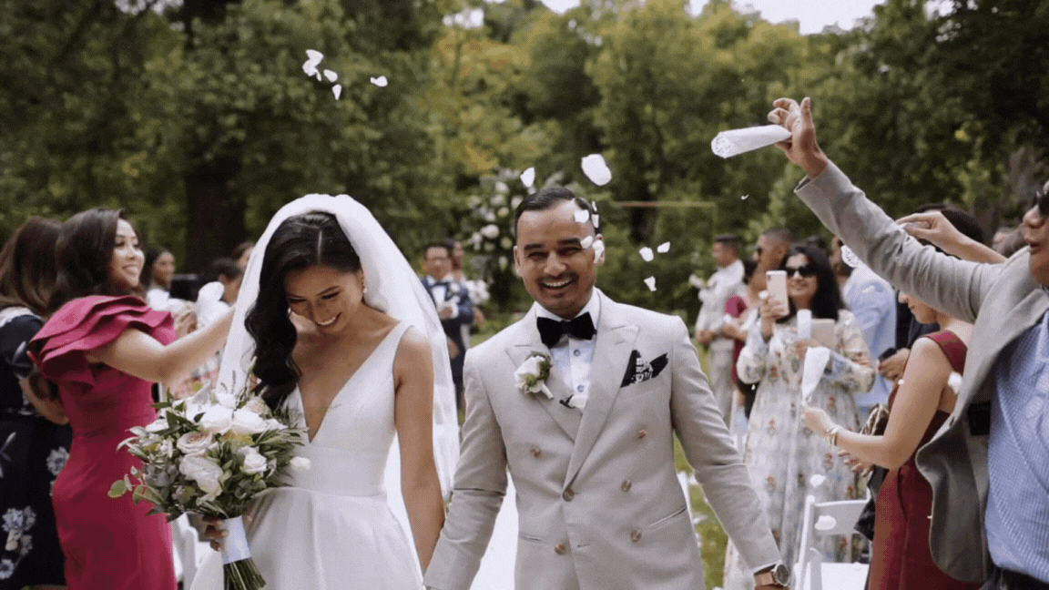 A moving image of a bride and groom walking down the aisle after being pronounced husband and wife being showered in rose petals with big smiles on their faces