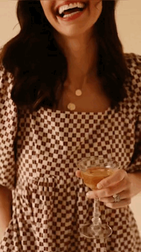 Video of a woman in a checkered dress smiling and holding a drink class