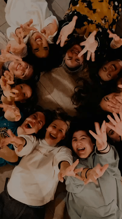 moving GIF of group of girls laying on the floor doing jazz hands up at the camera