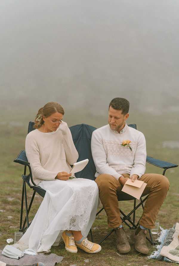 A portrait of a bride and a groom reading their vows while sitting on picnic chairs in Alaska