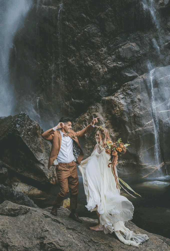 A bride and groom dance near a Yosemite waterfall as her dress flows in the wind during their small wedding.