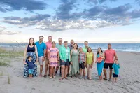 A large family stands together on the beach, dressed in vibrant, colorful outfits. The bright sky and ocean add to the cheerful atmosphere, ideal for destination family photographer NC, capturing lively and joyful family connections.