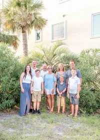 A multi-generational family stands together by palm trees, dressed in casual summer clothes. The bright greenery and relaxed expressions highlight their close-knit bond. Perfect for professional family photography in NC, showcasing family unity and happiness.
