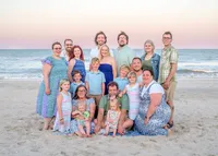 A multi-generational family poses on the sandy shores of Wrightsville Beach, dressed in coordinated blue and khaki outfits. The ocean waves and clear sky provide a beautiful backdrop, capturing the warmth and connection of family. Ideal for North Carolina family photography, highlighting beachside gatherings.