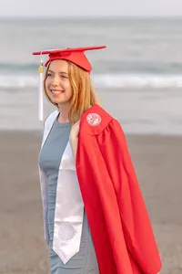 A college senior in a red cap and gown smiling by the ocean in Ocean Isle Beach, North Carolina. This vibrant portrait highlights the joy of graduation, perfect for capturing memorable senior moments on the beach.