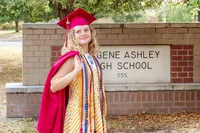A proud graduate in a red cap and gown posing in front of Eugene Ashley High School in Wilmington, NC. This image captures the excitement of graduation, perfect for seniors looking for affordable graduation photography in Wilmington.
