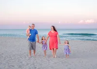 A family of five walks hand in hand along Carolina Beach at sunset, dressed in vibrant summer attire. The pastel sky and gentle waves create a serene backdrop. Perfect for artistic family photography in Wilmington, NC, highlighting joyful family moments.