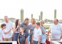 A family shares a joyful moment at a marina, with boats and dock posts in the background. Dressed in casual summer attire, they enjoy a relaxed atmosphere. Perfect for North Carolina family photography, capturing candid and happy interactions by the water.