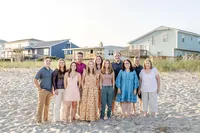 A family stands on the sandy beach in front of colorful coastal homes. Dressed in casual summer outfits, they enjoy a sunny day by the sea, ideal for professional family photography in NC, showcasing vibrant beachside gatherings.