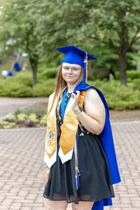 A Cape Fear Community College senior proudly wearing a blue cap and gown with honor cords, standing on a brick path in North Carolina. This image celebrates academic achievement, ideal for those looking for professional graduation photography.