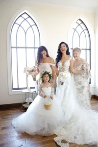 Bride with her flower girl and bridesmaids beside Gothic arched windows