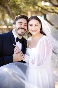 Laughing bride and groom in black tie as her veil sweeps across the frame