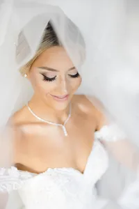 Close-up bridal portrait framed by a sheer veil and a diamond necklace