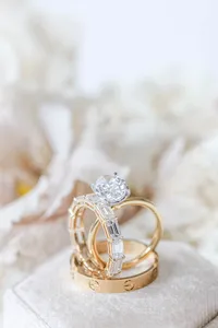 Diamond engagement ring stacked with gold wedding bands against soft ivory florals