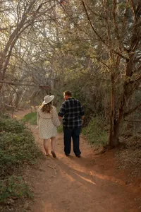 Couple walking hand-in-hand along a wooded trail during their Lover's Knoll engagement session