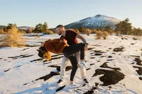 Man playfully twirling his partner in the snow at sunset during their engagement session