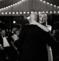 Bride embraces her father during a first dance at The Club at 12 Oaks, guests watching beneath draped café lights.