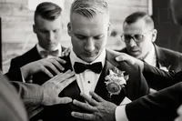 A documentary wedding photography shot of a groom being helped by his groomsmen, focusing on the genuine connection of the wedding party.
