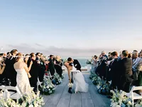 A celebratory dip kiss between a bride and groom on a rooftop overlooking the ocean at Wychmere Beach Club in Cape Cod.