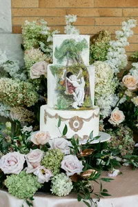 A three-tier luxury wedding cake featuring intricate hand-painted classical art and a base of lush summer roses.