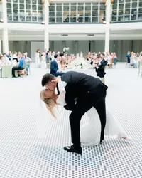 Groom dips his bride during their first dance in a bright circular ballroom as guests look on from surrounding tables at Dayton Arcade wedding.