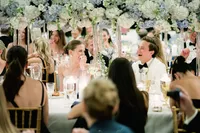 Couple laughing together at their reception table beneath a canopy of white and blue florals as guests smile around them.