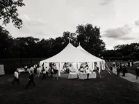White sailcloth tent set on an open lawn during a summer wedding in Bedford, New York as guests mingle at dusk.