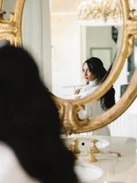 An intentional imagery capture of a bride’s reflection in an ornate gold mirror, showcasing a quiet, natural unfolding of the day.