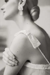 Close-up black and white film-style photograph of a bride's shoulder and pearl-detailed strap, emphasizing a timeless and authentic aesthetic in Paris, France.