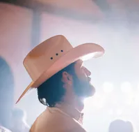 Groom in a cowboy hat looks toward the dance floor during an Asheville wedding reception, lights softly flaring behind him.