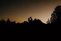 man and woman are seen in a silhouette with the grand tetons behind them