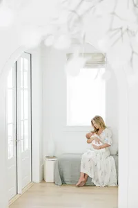 a mother and her baby sitting in a bright room and cuddling with each other