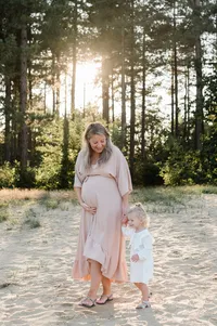 Een intiem moment tussen een zwangere moeder en haar dochter tijdens een fotoshoot in de natuur bij zonsondergang, vastgelegd door Monica Stout Fotografie.