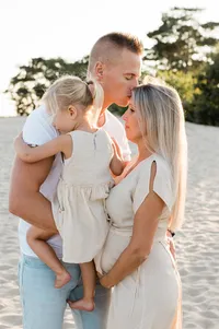 Een zwangerschapsfotoshoot op het strand, waar een moeder liefdevol met haar gezin poseert, gefotografeerd door Monica Stout Fotografie.