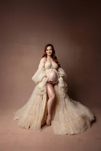 Studio maternity portrait of a pregnant woman in a flowing champagne tulle gown gently holding her baby bump, photographed by Yucaipa maternity photographer Kaitlyn Dawn Photography.