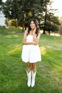 High school senior girl standing on a grassy lawn wearing a white dress and boots, natural outdoor senior portrait by Kaitlyn Dawn Photography.