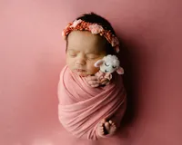Sleeping newborn baby girl wrapped in a pink swaddle and holding a small plush lamb prop during a studio newborn photography session in Inland Empire by Kaitlyn Dawn Photography.