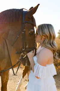 High school senior girl gently holding a horse in a sunlit field, lifestyle senior portrait session by Kaitlyn Dawn Photography.