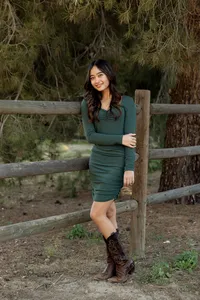 High school senior girl posing by a wooden fence in a green dress and cowboy boots, outdoor senior photos by Inland Empire senior photographer Kaitlyn Dawn Photography.