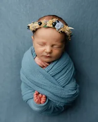 Sleeping newborn baby wrapped in a soft blue swaddle and wearing a floral headband during a studio newborn photography session with newborn photographer Kaitlyn Dawn Photography.