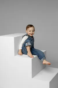 Young girl sitting barefoot on white studio blocks with a soft gray background, natural light studio child portrait photographed by Kaitlyn Dawn Photography.