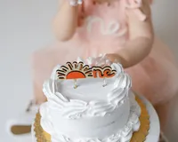 Close-up of white cake with sunrise “one” topper during cake smash session. Photograph by Yucaipa cake smash photographer Kaitlyn Dawn Photography.