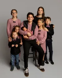 A portrait of five siblings and a sleeping newborn baby posed together in a studio during a professional newborn photography session in Inland Empire by Kaitlyn Dawn Photography.