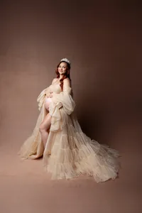 Studio maternity portrait of a pregnant woman wearing a champagne maternity gown and crown, smiling at the camera while holding her baby bump, photographed by Kaitlyn Dawn Photography.
