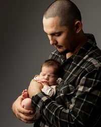 Father holding his sleeping newborn baby during a heartfelt studio newborn portrait session by Kaitlyn Dawn Photography.