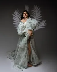 Fine art pregnancy portrait of a pregnant woman wearing a flowing green maternity gown with soft botanical light patterns photographed by Kaitlyn Dawn Photography.