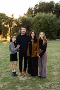 Father and mother standing with two teenage daughters in a park at sunset, coordinated neutral outfits captured by Kaitlyn Dawn Photography, professional family portrait photographer.