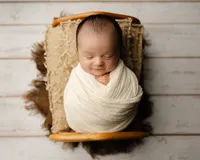 Sleeping newborn baby wrapped in a cream swaddle and posed in a wooden prop bed during a studio newborn photography session with newborn photographer Kaitlyn Dawn Photography.