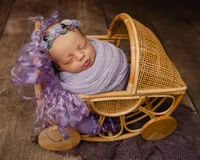 Sleeping newborn baby girl wrapped in a lavender swaddle and posed in a vintage wicker stroller prop during a studio session with newborn photographer Kaitlyn Dawn Photography.