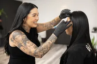 Tattooed beauty professional smiling while styling a client’s brows. Photograph by Yucaipa branding photographer Kaitlyn Dawn Photography.